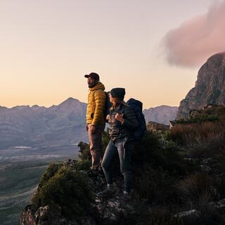 Two hikers standing on a rocky mountain watching a sunset