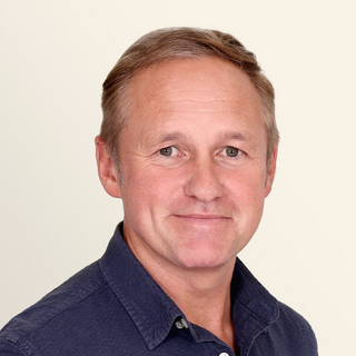 Lighthouse CEO Sean Fitspatrick with short light brown hair and a blue collared shirt is smiling in front of a neutral background.